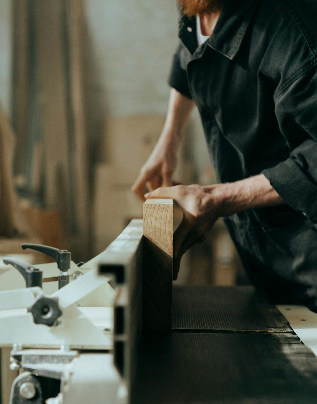 Un menuisier guide une pièce de bois sur une machine d'atelier